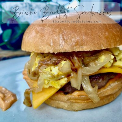 Brioche Breakfast Sandwiches -- a soft brioche bun surrounding melty cheese, thick cut Canadian bacon or a savory sausage patty topped with the creamiest scrambled eggs you've ever had, finished with caramelized onions and the perfect hint of flavor and heat in a swipe of sriracha mayo. | thatwhichnourishes.com
